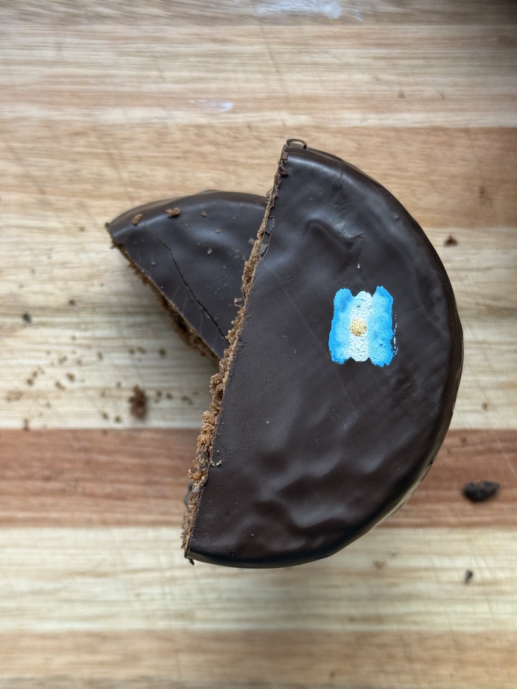 Un alfajor de chocolate cortado al medio sobre la mesada de madera.