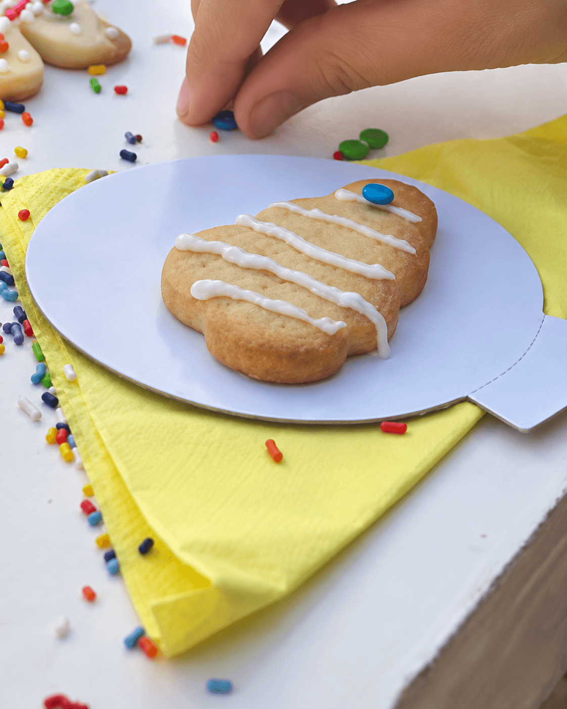 Una mano coloca una gragea de color sobre una galletita glaseada, en la mesa de una clase.
