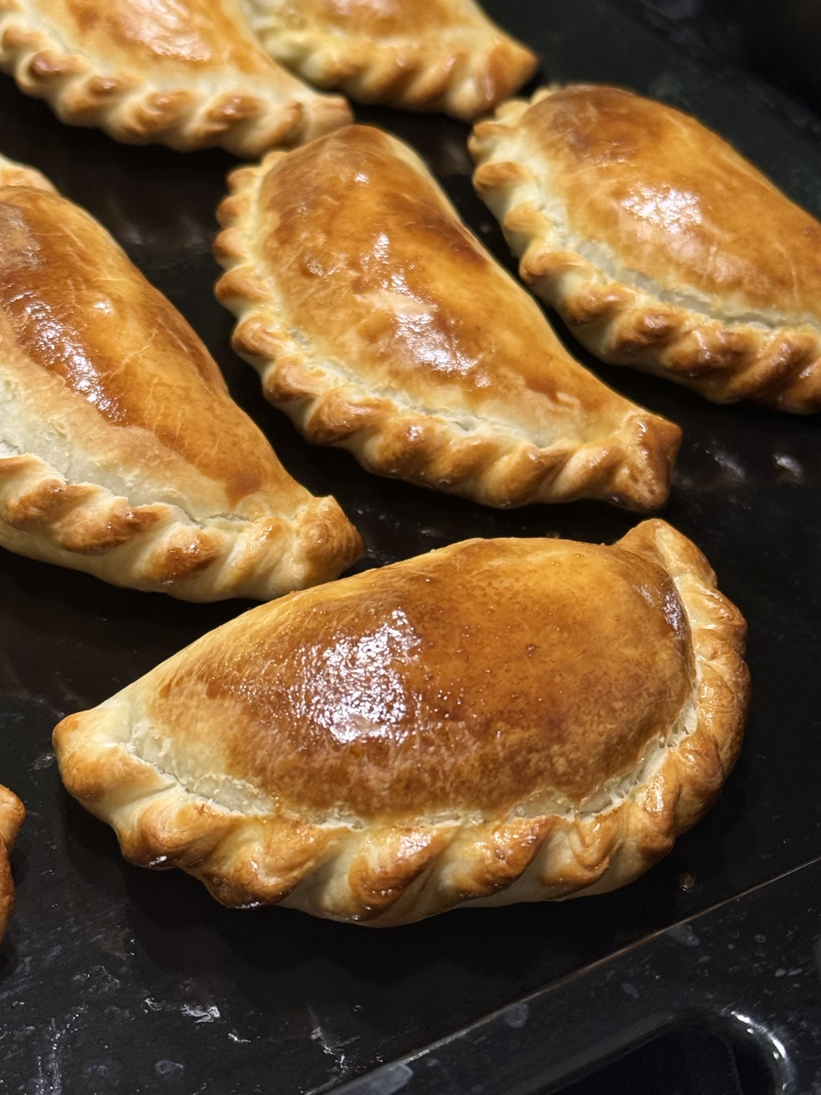 Empanadas repulgadas a mano, doradas, sobre la placa del horno.