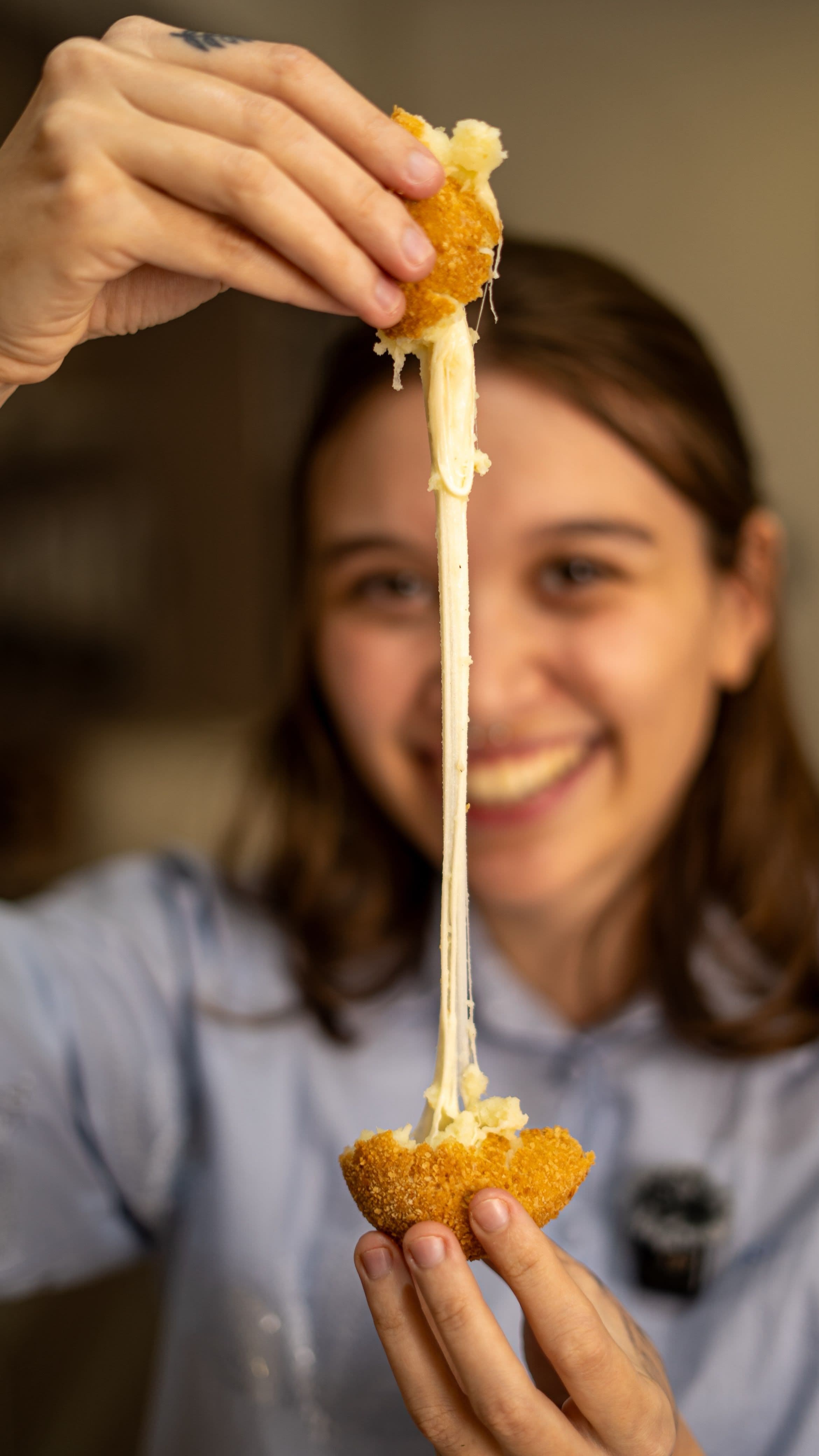 Delfina sonriendo mientras estira el queso de una croqueta recién partida.