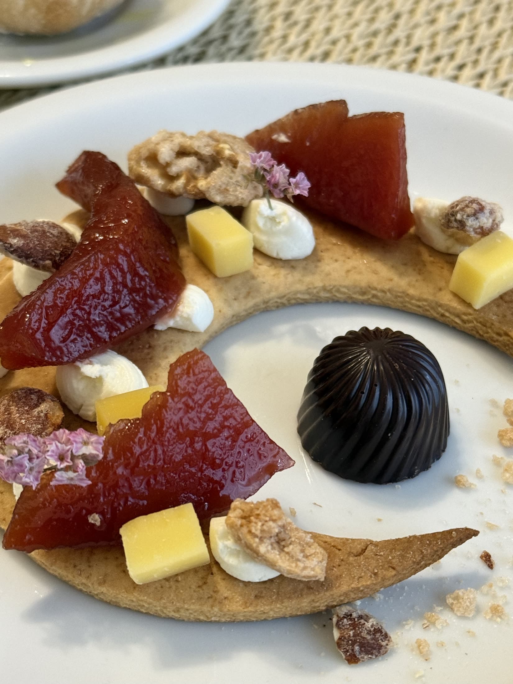 Postre emplatado con membrillo, queso, nueces y un bombón de chocolate.