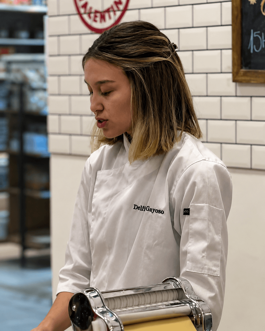 Delfina pasa la masa por la máquina de pastas mientras explica, en plena clase.