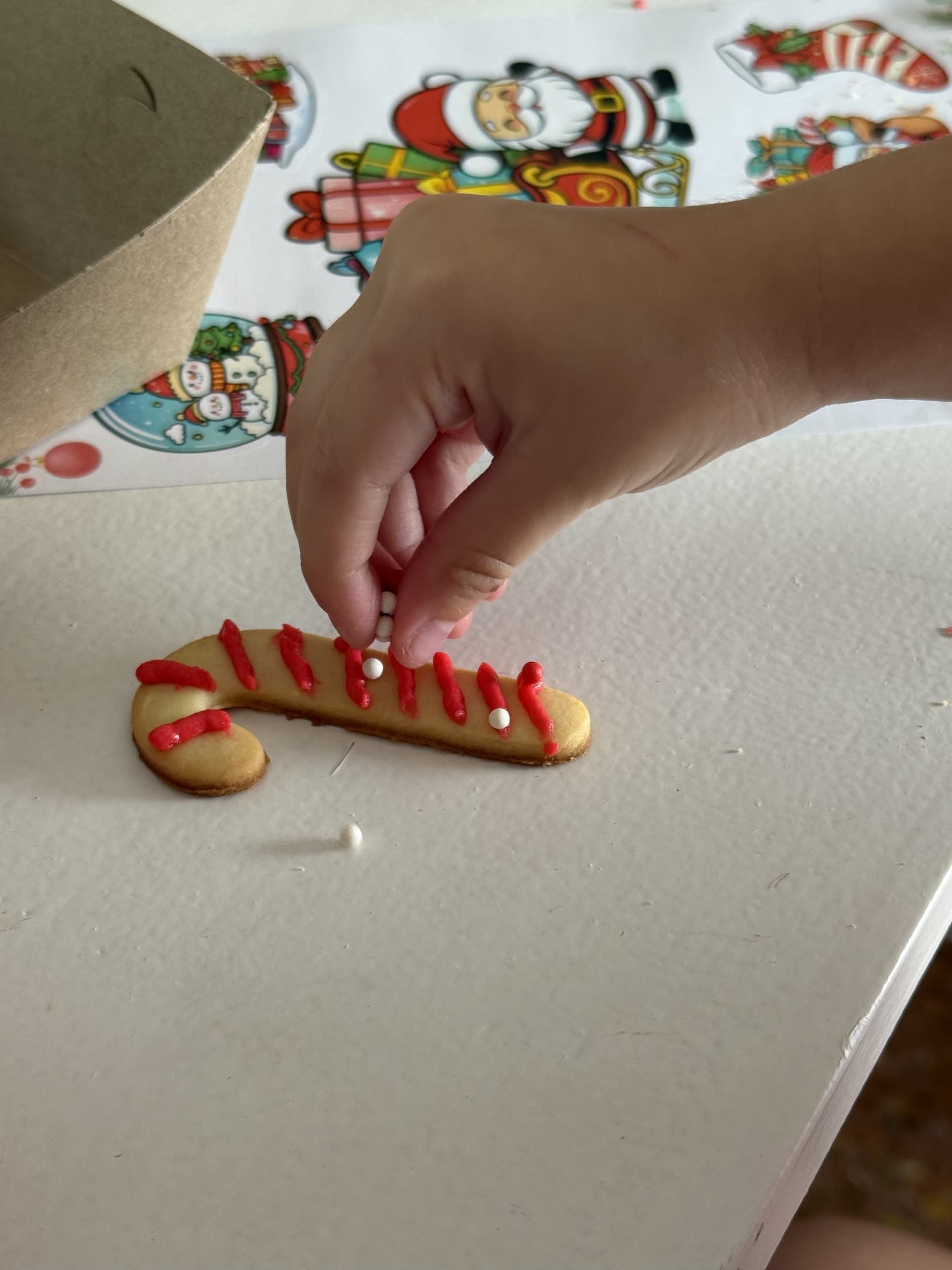 Una mano dibuja con glasé rojo sobre una galletita alargada.