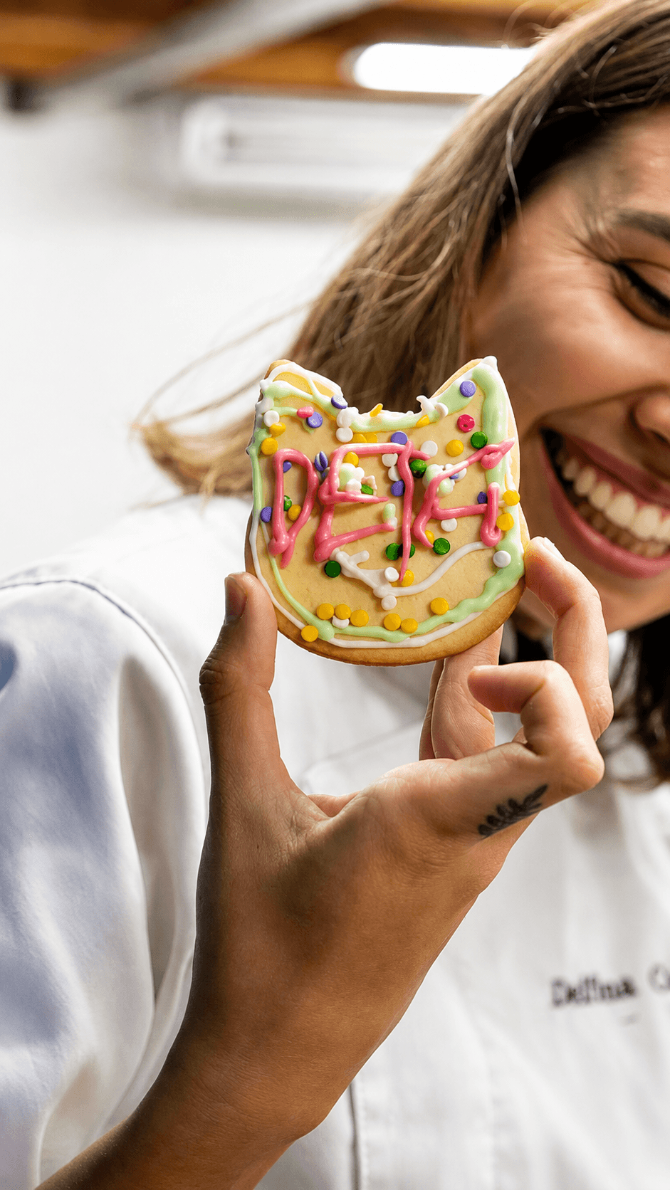 Delfina se ríe mientras sostiene una galletita con forma de gato decorada con glasé que dice "Delfi".